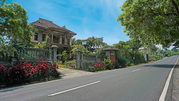 A two-story house with a tiled roof, surrounded by a stone wall and lush greenery. - SPOT ON 91527 As-sakinah Homestay Syariah (Surabaya)