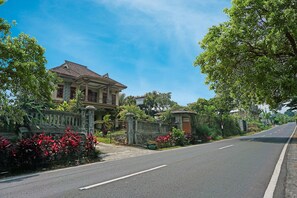 A two-story house with a tiled roof, surrounded by a stone wall and lush greenery. - SPOT ON 91527 As-sakinah Homestay Syariah (Surabaya)
