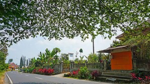 A road lined with lush greenery and a traditional building with a red door. - SPOT ON 91527 As-sakinah Homestay Syariah (Surabaya)