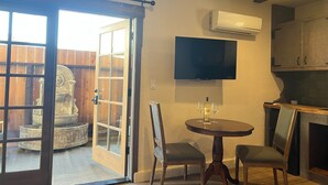 Una habitación con puerta corrediza de vidrio que da a un patio, una mesa redonda con sillas, un televisor de pantalla plana montado en la pared y una chimenea.