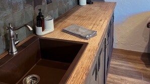 Una cocina con encimera de madera, un fregadero, una cafetera y una ventana con persianas.