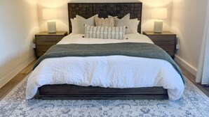 Una cama bien tendida, con un cabecero oscuro, dos mesitas de noche con lámparas y una alfombra estampada.
