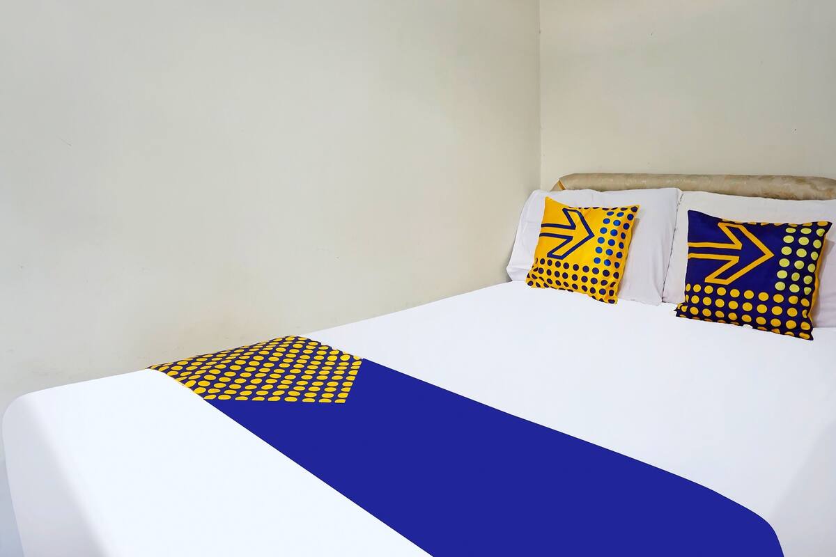 Ein Bett mit weißblauer Bettdecke, zwei Kissen mit gelbblauen Mustern und einer schlichten Wand.