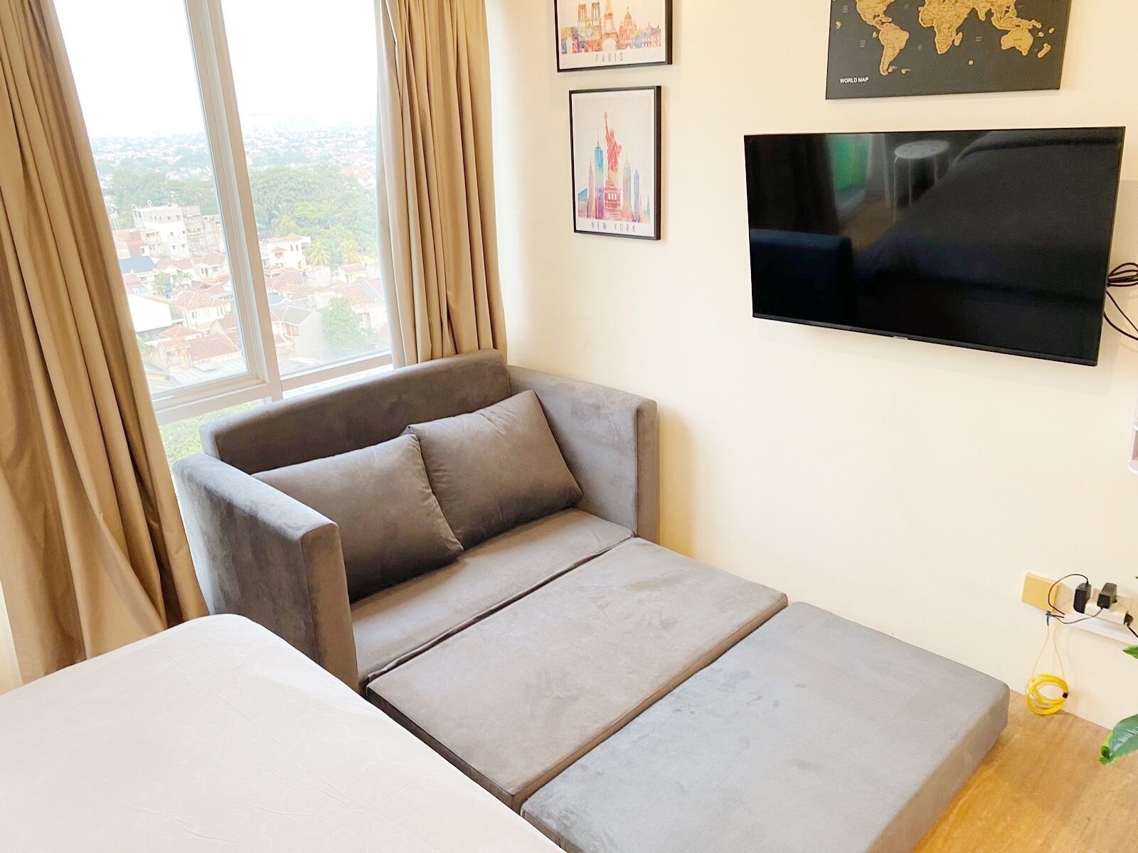 Una stanza con un divano grigio, una TV a schermo piatto montata a parete e una finestra con tende.