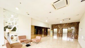 Eine geräumige Lobby mit modernem Design, inklusive einer Sitzecke mit zwei Sesseln und einem kleinen Tisch, einer Wand mit abstrakten Mustern und einem Marmorboden.