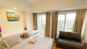 Ein Schlafzimmer mit einem großen Bett, einer Couch, einem Gemälde und Blick auf Gebäude durch das Fenster.