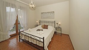 A bedroom with a bed, two bedside tables, a chandelier, a window with curtains, and a painting on the wall. - Casa Pel r in Toscolano Maderno (Toscolano Maderno)