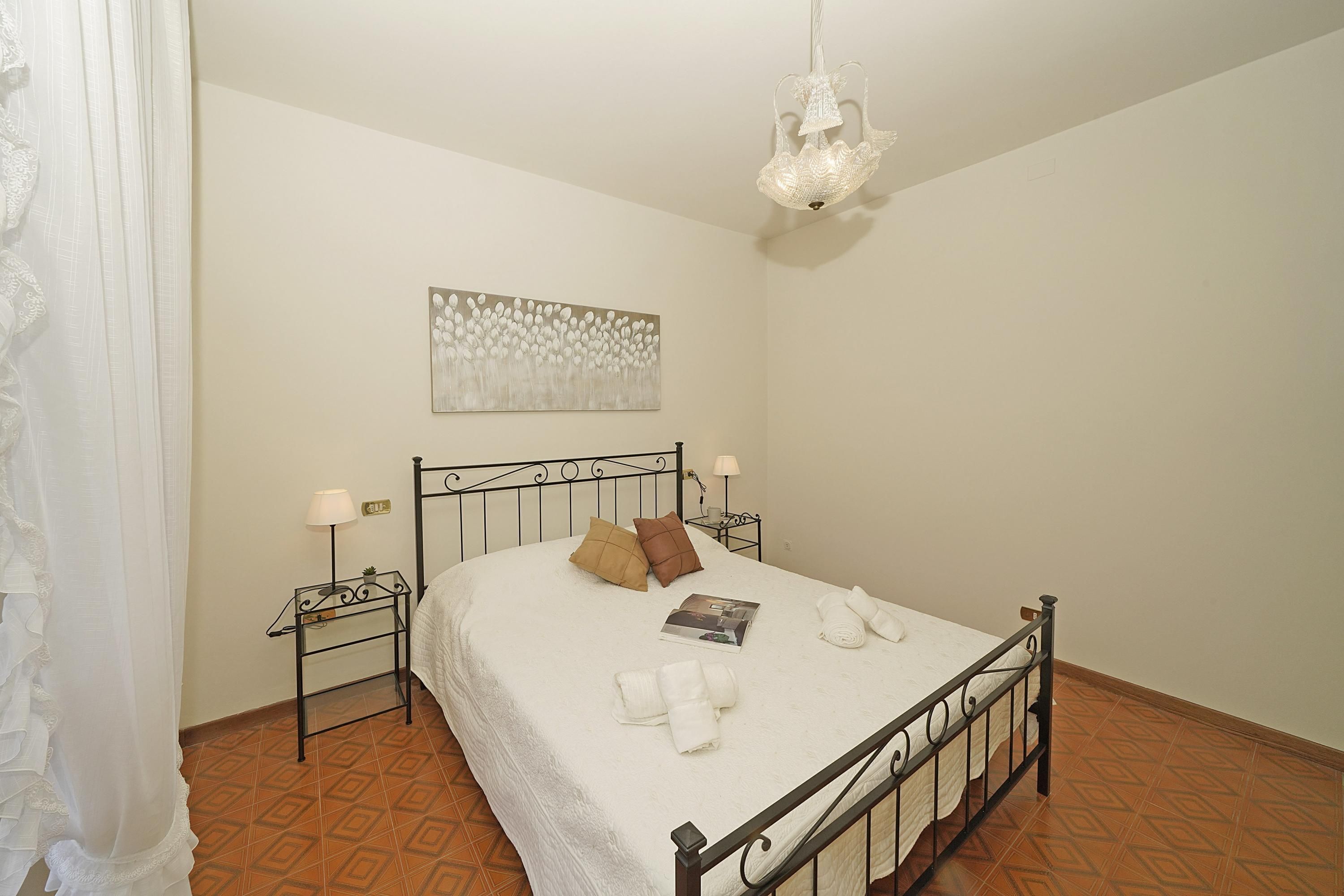 A neatly made bed with pillows, a bedside table with a lamp, and a wall art piece.