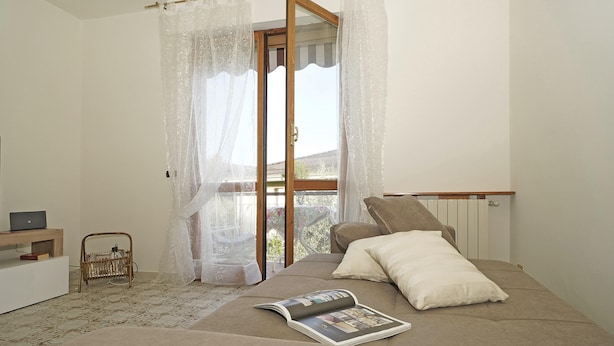 A bedroom with a bed, a magazine on the bed, a laptop on a side table, and a window with sheer curtains. - Casa Pel r in Toscolano Maderno (Toscolano Maderno)