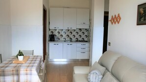 A compact living space with a dining area, kitchenette, and a sofa with a decorative pillow. - Appartamento Anna 701 (Tignale)