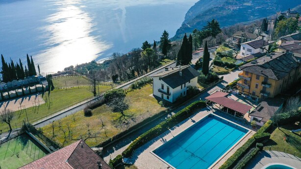 An aerial view of a residential area with a swimming pool, houses, and a view of a lake. - Appartamento Anna 701 (Tignale)