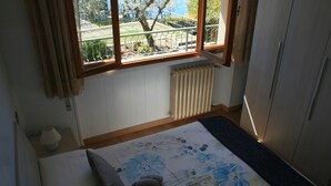 A bedroom with a bed, a window with a view of a garden, a radiator, and a wardrobe. - Appartamento Anna 701 (Tignale)