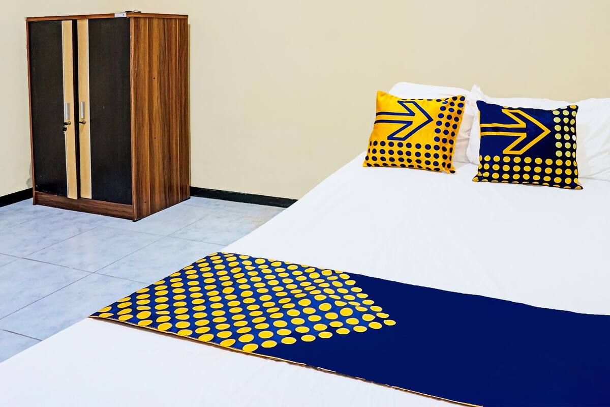 A bedroom with a bed, pillows, a wooden wardrobe, and a patterned rug.