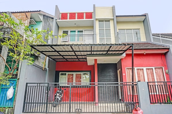 A multi-story residential building with a red facade, a balcony, and a gated entrance.