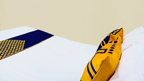 A bed with a white sheet and a pillow with a yellow and blue design. - OYO Life  92091 Citra Omah Syariah (Malang)