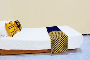 A single bed with a white mattress, two yellow pillows with blue patterns, and a blue and yellow polka dot blanket.