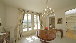 A dining room with a wooden table, a chandelier, and a view of the outdoors through large windows. - Villa San Carlo in Ro (Roe Volciano)