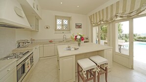 A kitchen with a central island, a stove, and a sink. There is a window with a view of the outdoors. - Villa San Carlo in Ro (Roe Volciano)