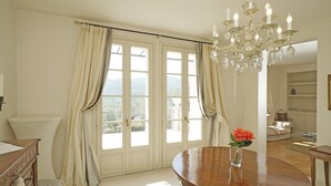 A spacious room with a large window, a wooden dining table, and a chandelier. - Villa San Carlo in Ro (Roe Volciano)