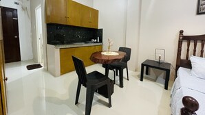 A compact room with a bed, a small table with chairs, a kitchenette, and a door. - Sto. Nino Residences (Lucena)