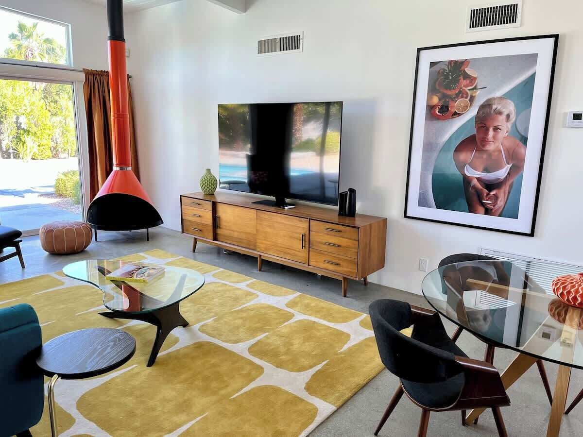 A modern living room with a TV, wooden cabinet, glass coffee table, and a framed picture on the wall.