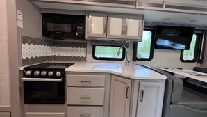 A compact RV kitchen with a stove, microwave, and a window offering a view of the outdoors.