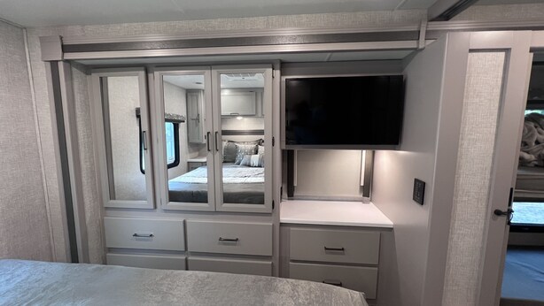 A bedroom with a bed, a wardrobe with mirrored doors, a television, and a bedside table.