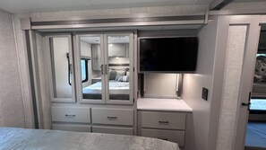 A bedroom with a bed, a wardrobe with mirrored doors, a television, and a bedside table. - Luxury RV with Bunkbeds Stationed on serene Grand River with private golf course (Grand Rapids)