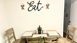 A dining area with a table set for four, surrounded by wooden chairs. Above the table, there is a wall-mounted sign that reads "Eat." - 4 Bed Large Backyard Near Airport & AT&T Stadium (Bedford)