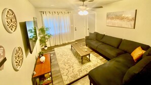 A living room with a sofa, a coffee table, a plant, and a painting on the wall. - 4 Bed Large Backyard Near Airport & AT&T Stadium (Bedford)