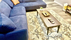 A modern living room with a blue sectional sofa, a wooden coffee table, and a patterned rug. - 4 Bed Large Backyard Near Airport & AT&T Stadium (Bedford)