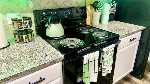 A kitchen with a black stove, white cabinets, and a microwave above. There are spice jars on the counter and a kettle on the stove. - 4 Bed Large Backyard Near Airport & AT&T Stadium (Bedford)