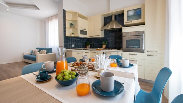 A modern kitchen with white cabinets, a built-in oven, and a dining area with a table set for breakfast. - Nida 18 in Cattolica (Cattolica)