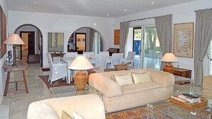 Un salon spacieux avec un canapé beige, une table basse et un coin repas comprenant des chaises et une table blanches.