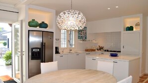 Une cuisine moderne avec des meubles blancs, un réfrigérateur en acier inoxydable, une table de salle à manger ronde et un lustre original.