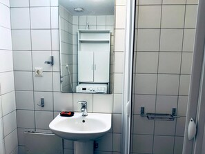Une salle de bain avec un lavabo blanc, un miroir, un meuble et un espace douche.