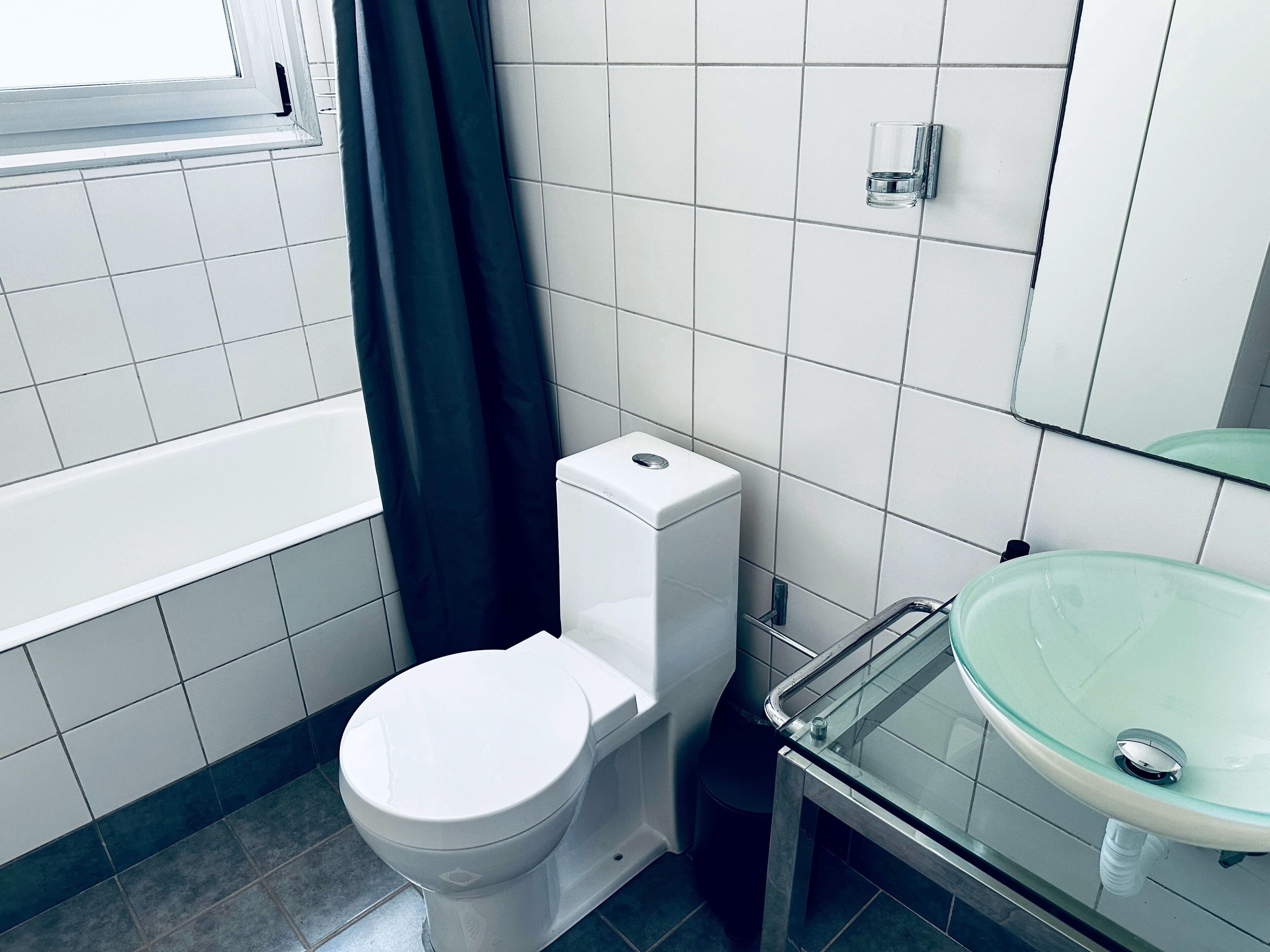 A bathroom with a toilet, a glass sink, and a window with a curtain.
