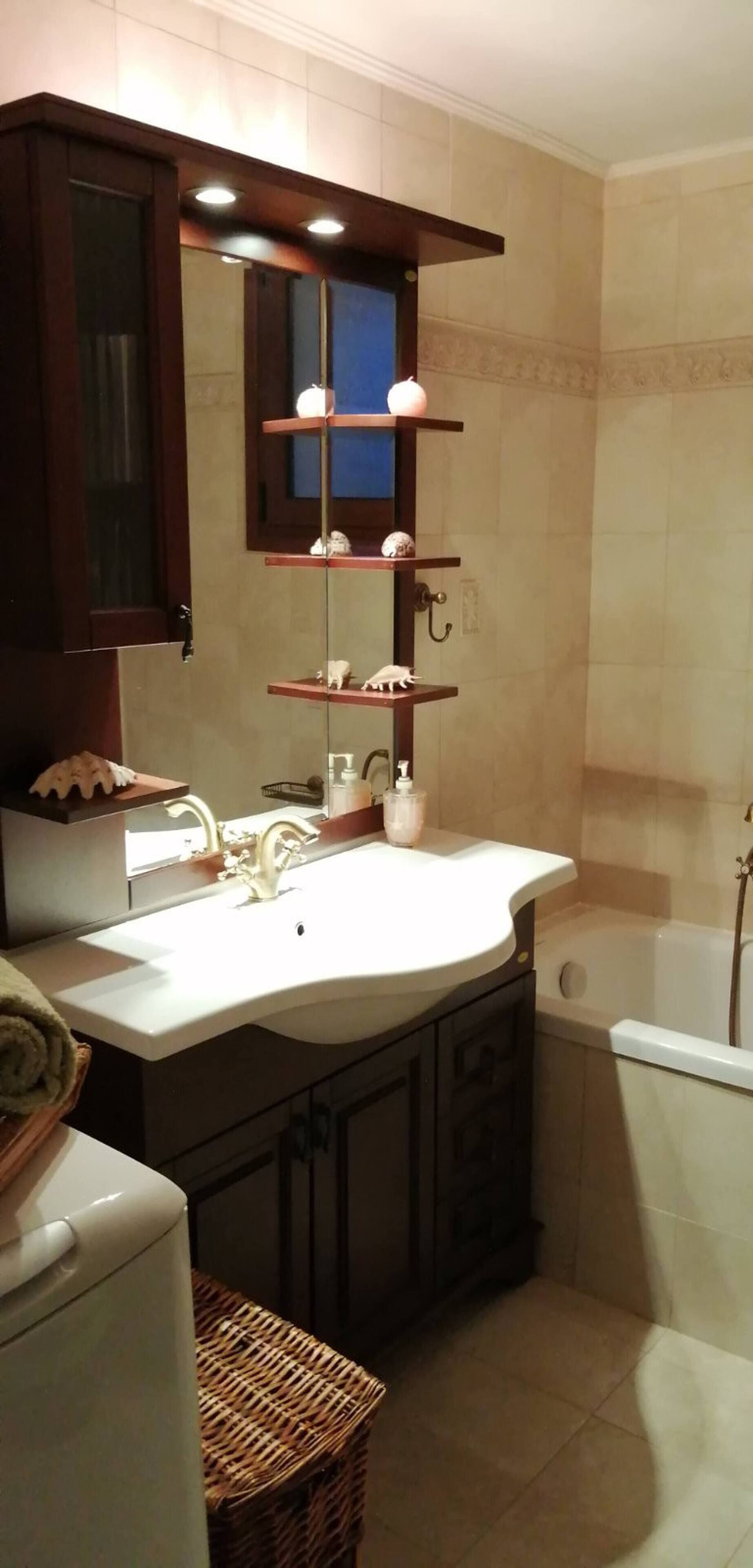 Un bagno con lavandino, specchio, scaffali con articoli da toilette, una vasca e un cesto in vimini.