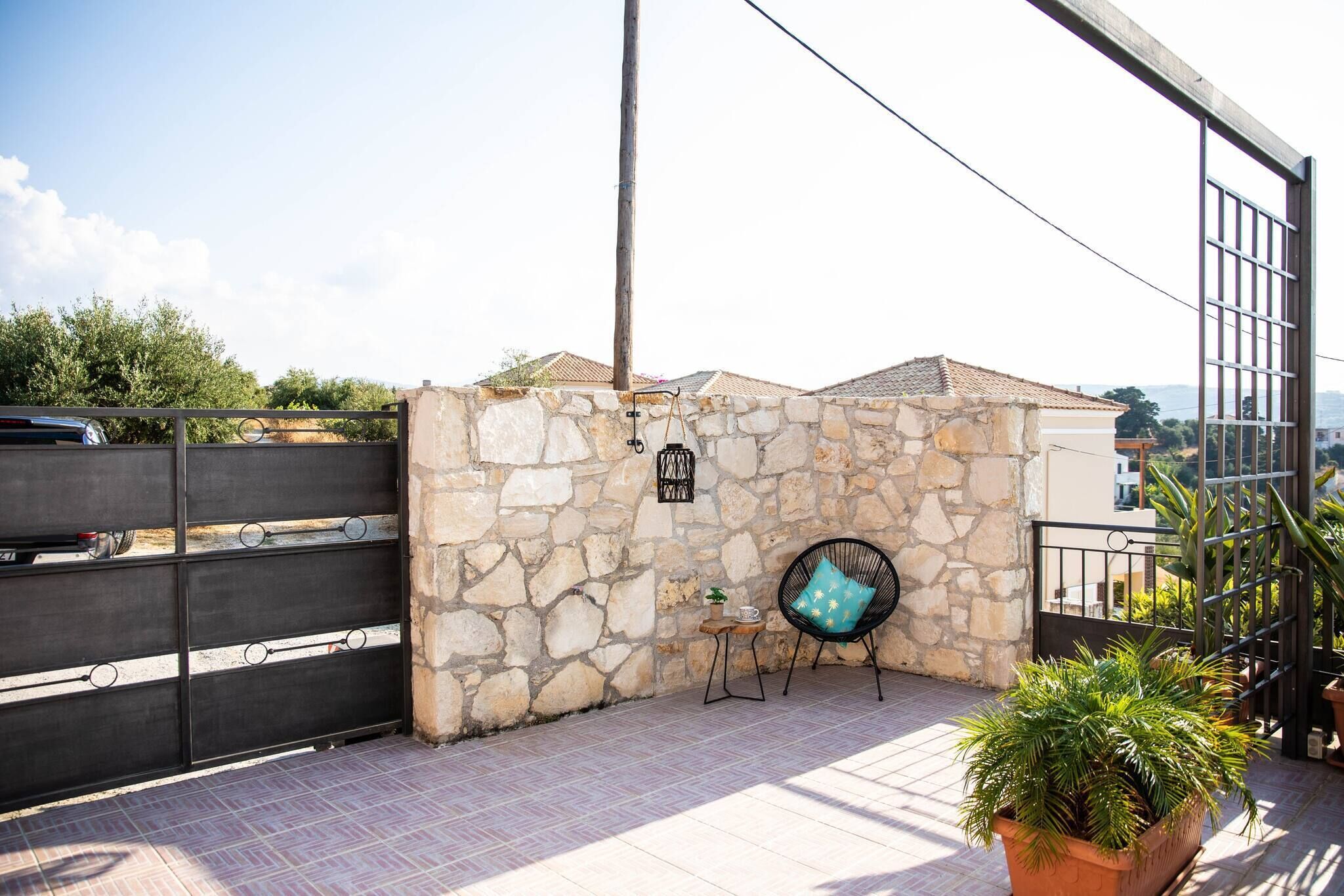 A stone wall with a metal gate, a potted plant, and a chair with a cushion.