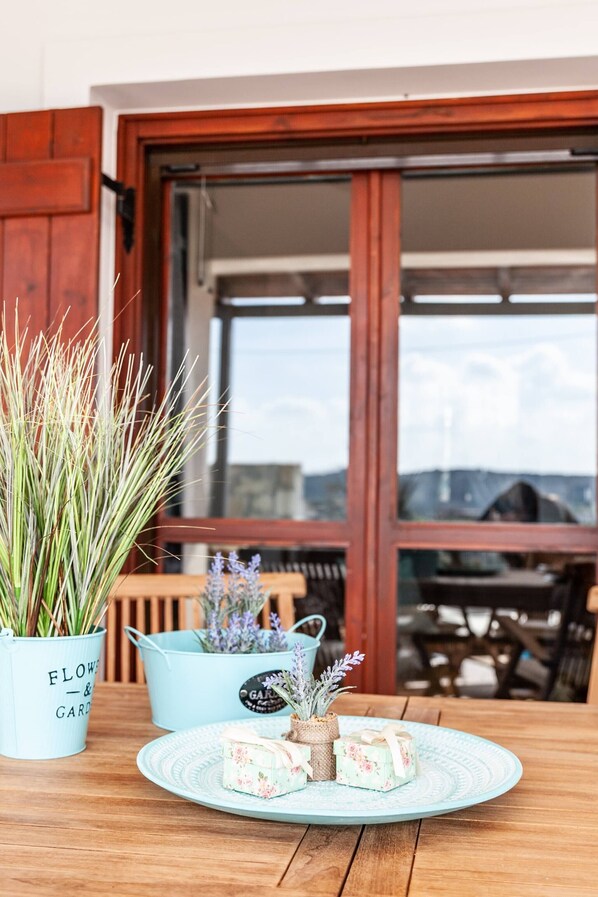 A wooden table with a plate of food, potted plants, and a view of a building through a window.