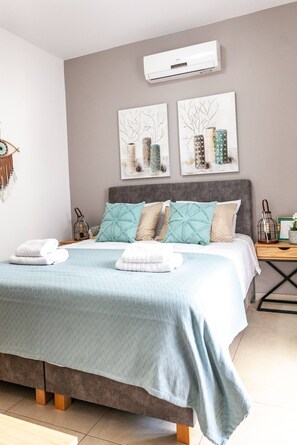 A bedroom with a bed, a bedside table, a wall-mounted air conditioner, and two wall art pieces.