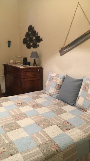 Un dormitorio con cama, cómoda, lámpara, decoración en la pared y colcha acolchada.