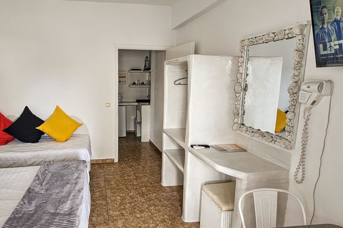 A hotel room with two beds, a desk, a chair, a mirror, and a bathroom visible in the background.