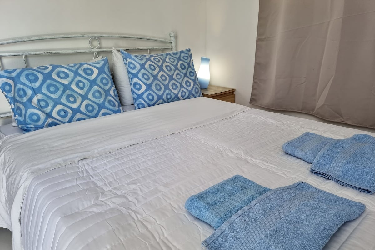 A neatly made bed with blue and white patterned pillows, a white quilted bedspread, and folded blue towels.