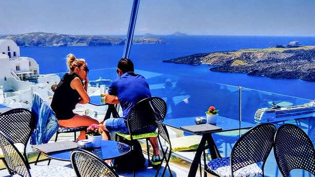 A couple dining at a table with a view of the sea and rocky islands. - Santorini Studios Pleasure By The Sea (Santorini)