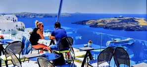 A couple dining at a table with a view of the sea and rocky islands. - Santorini Studios Pleasure By The Sea (Santorini)