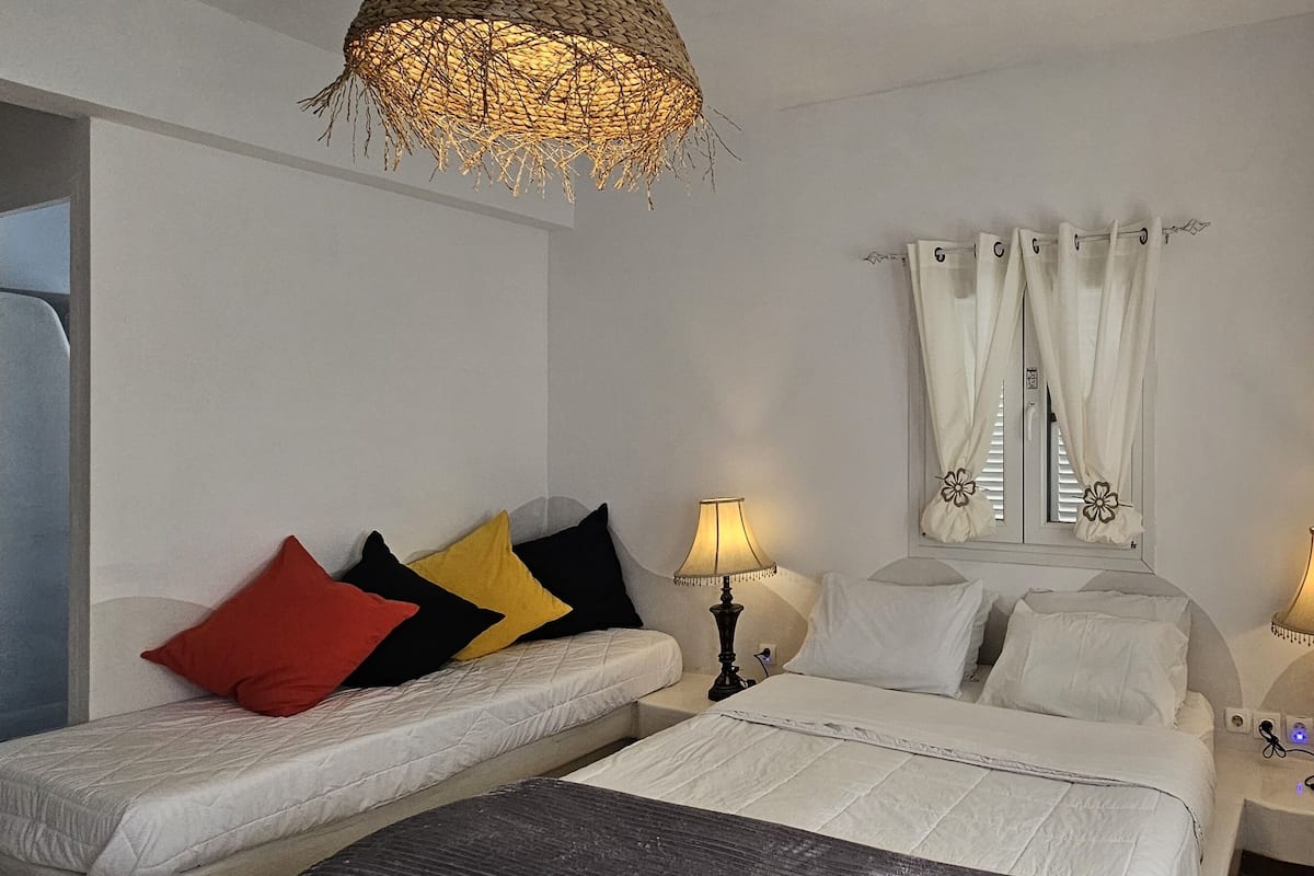 A bedroom with a bed, two bedside tables with lamps, a sofa with pillows, and a decorative ceiling light.