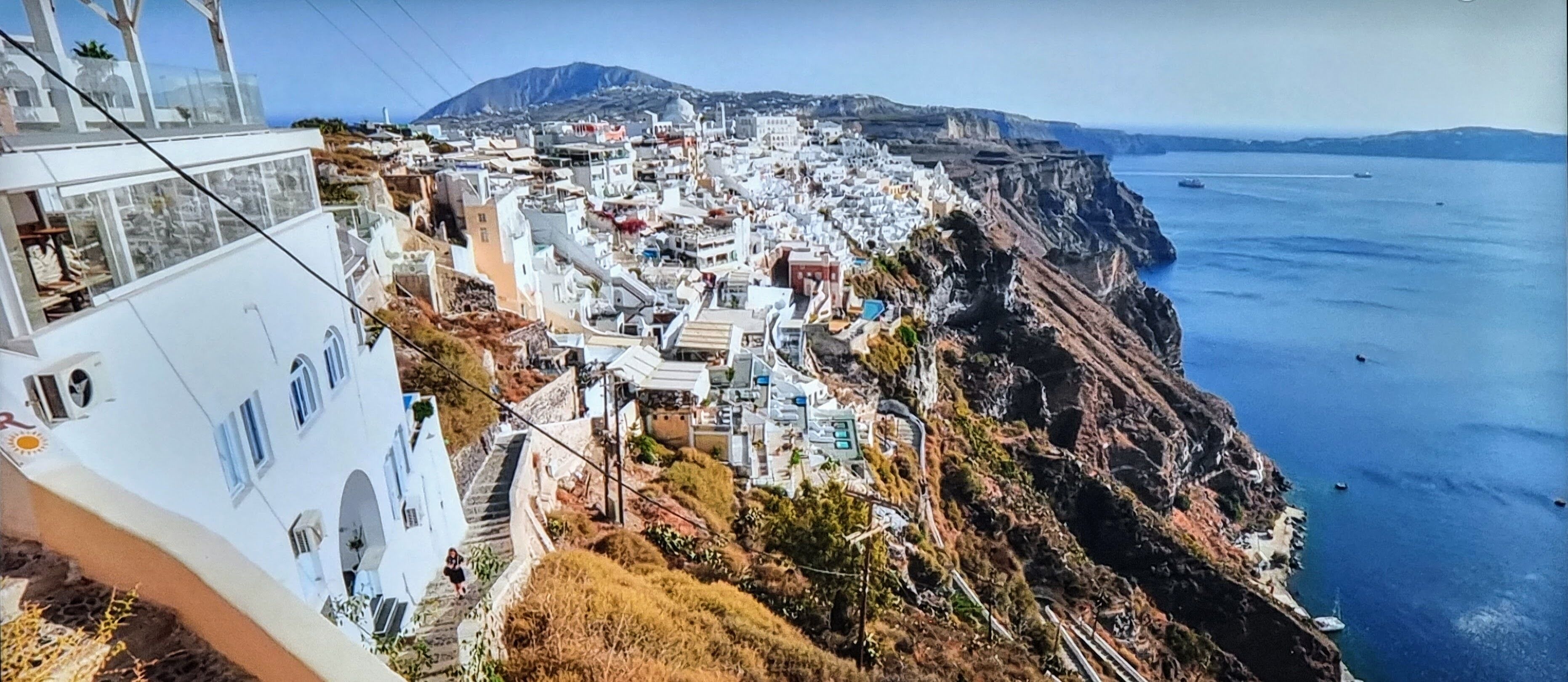 A coastal town with buildings along the cliffside, a clear view of the sea, and a mountain in the background.