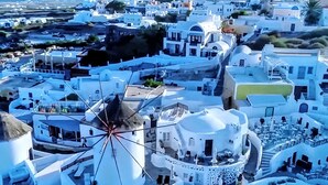 A coastal town with white buildings, a prominent windmill, and a clear view of the sea. - Santorini Studios Pleasure By The Sea (Santorini)