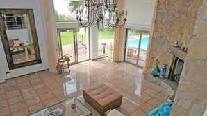 A spacious living room with a large glass table, a brown sofa, and a stone fireplace. - Villa zu Vermieten in Porto del Almendros, Los Arqueros, Benahavis (Benahavís)